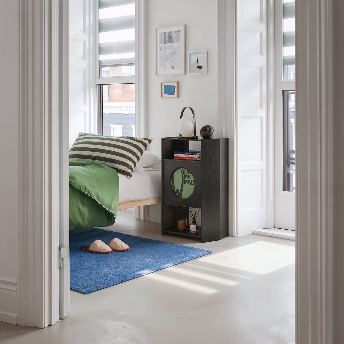 FITUEYES Picasso RS05 vinyl storage cabinet with headphones beside a bed with green bedding and a blue rug