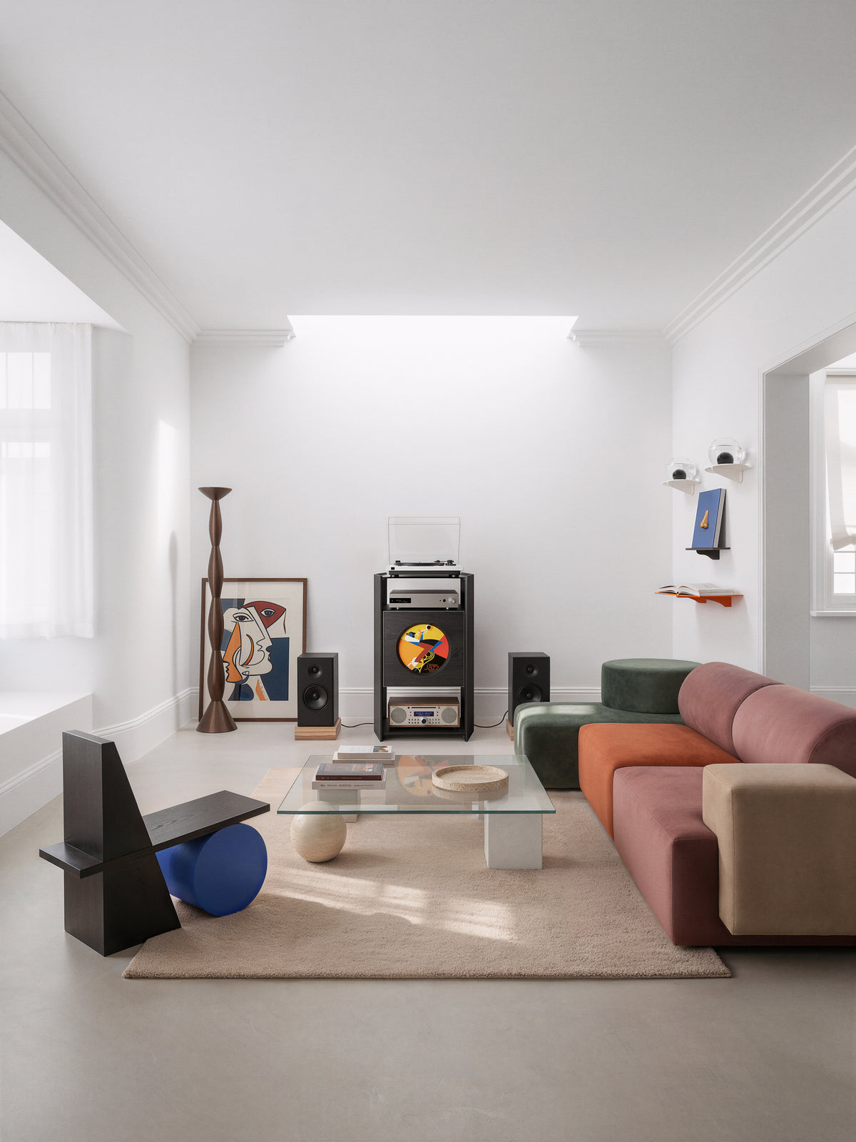 Black Picasso RS05 turntable stand between speakers in a bright living room with a multicoloured sofa