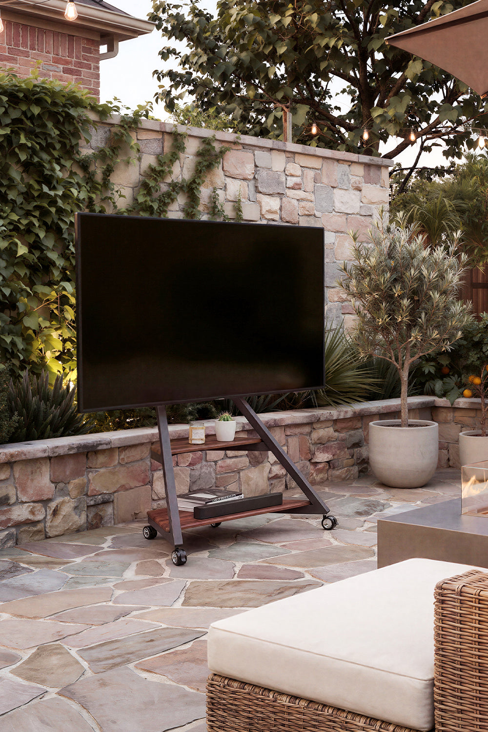 Outdoor television on a freestanding TV stand in a stone-walled garden seating area